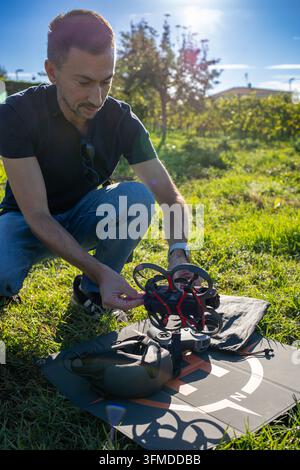 Man crouching on grass setting up a modern FPV drone and goggles on a landing pad, ready for an immersive first person view flying experience outdoors Stock Photo