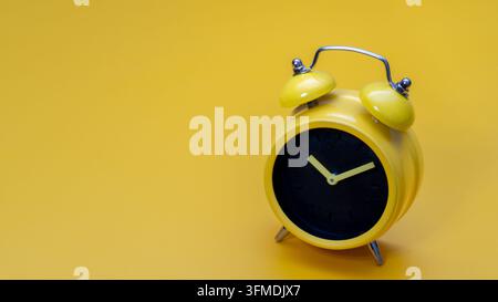 Yellow retro alarm clock against a yellow background with copy space. Time management, scheduling, urgency, deadlines, and morning routines concept. Stock Photo