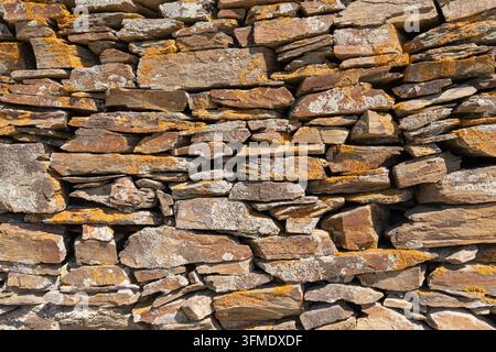 Close-up of a rustic dry stone wall showcasing layered natural rocks and weathered textures suitable as a background Stock Photo