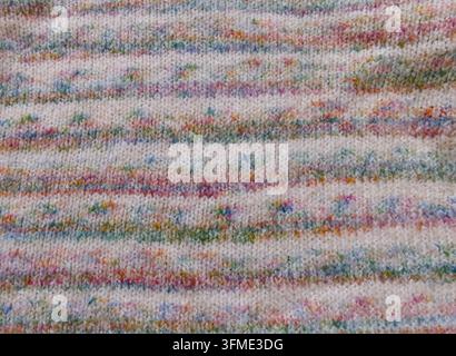 Cozy knitted fabric close-up featuring subtle horizontal stripes and colorful speckles for textile and fashion design. Stock Photo