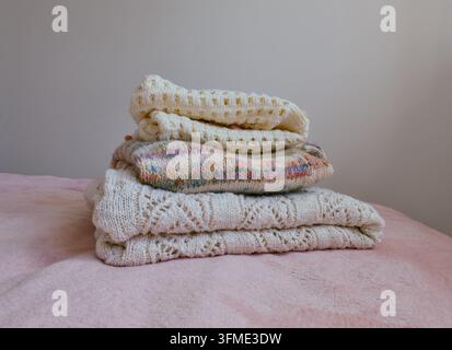 Tidy stack of soft hand-knitted garments in various patterns and colors on a plush pink blanket. Stock Photo