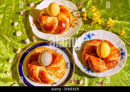 Three Easter wreaths with colored Easter eggs on colorful plates on green crinkle tablecloth with daisies and forsythia branch Stock Photo