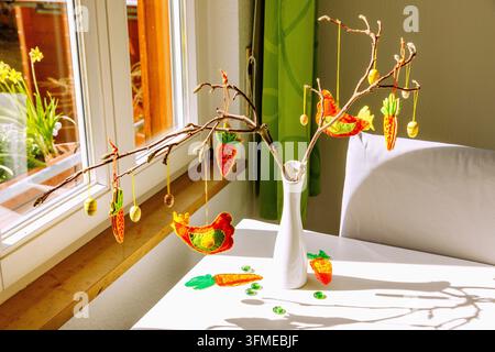 Easter decoration on white dining table with white vase and branches, hung with small wooden Easter eggs, felt carrots and homemade felt chickens, vie Stock Photo