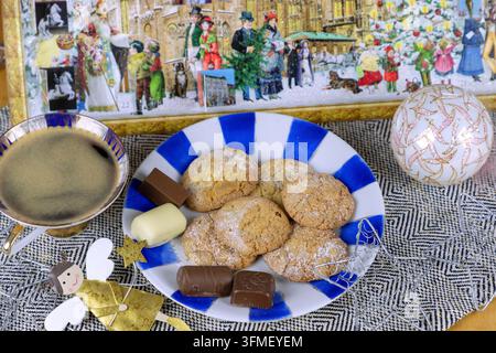 Orange cookies with chocolate candy on plate and cup of coffee, arranged with golden angel figure, silver stars, Christmas ball and advent calendar Stock Photo