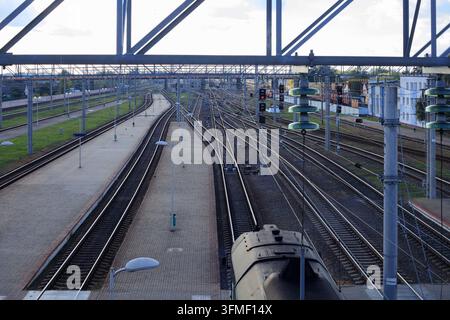 Overhead electric power lines and steel railway tracks for industrial electrification and energy concept. High voltage catenary grid system above outd Stock Photo