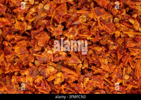 Crushed red pepper flakes, including dried chili pieces and seeds, creating a vibrant red and orange textured background, perfect for culinary and sea Stock Photo