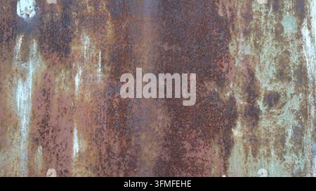 the texture of heavily corroded old metal. The surface is covered with a solid layer of reddish-brown rust, through which traces of faded greenish Stock Photo