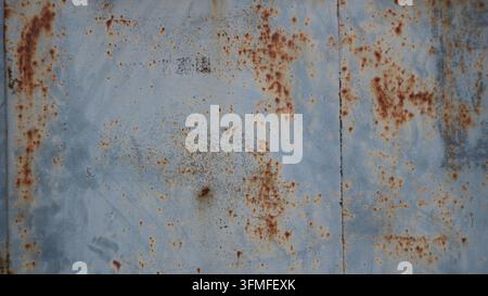 A background of aged sheet metal with a distressed texture. The metal surface features faded gray-blue enamel, random scratches, localized spots Stock Photo