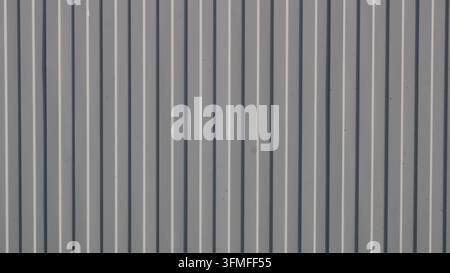 A background of vertical gray corrugated metal sheeting. The surface features a distinct geometric relief with alternating raised ribs and shadows Stock Photo