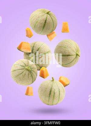 Fresh cantaloupe melons falling on violet background. Whole and sliced Stock Photo