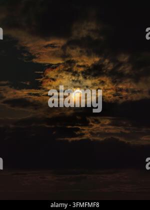 Partial solar eclipse revealing a glowing crescent of the sun peeking through heavy, dark clouds, capturing a rare celestial event and the awe inspiri Stock Photo