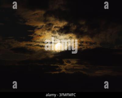 Partial solar eclipse creating a dramatic sky scene with sunlight peeking through dark, dense clouds, signifying celestial event, changing light, and Stock Photo