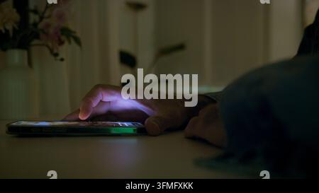 Person's hand interacting with a glowing smartphone screen displaying a social media feed, highlighting technology use and digital connection in a dar Stock Photo