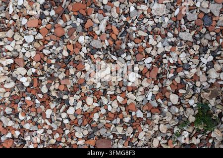 Close-up top view of a textured ground surface covered in small multicolored pebbles, grey gravel, and broken pieces of red terracotta bricks. Stock Photo