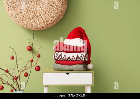 Christmas preparation and winter comfort, stack of warm knitted sweaters with a Santa hat on a bedside table in a cozy home interior Stock Photo