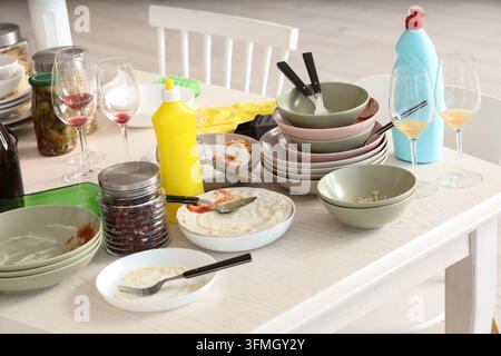 Household chores and messy kitchen, dirty dishes and food leftovers on dining table after dinner party with cleaning supplies and wine glasses Stock Photo