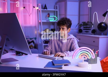 Digital childhood and remote learning, boy using computer for online education and gaming in bedroom with neon lighting at night Stock Photo