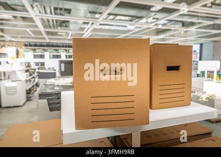 Two brown cardboard storage boxes with integrated handles sitting on a white retail display shelf inside a large furniture warehouse store, representi Stock Photo