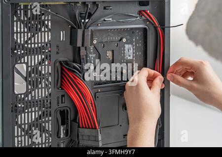 Close-up view of a technicians hands organizing and securing power and data cables inside a desktop case during a professional custom PC build, highli Stock Photo