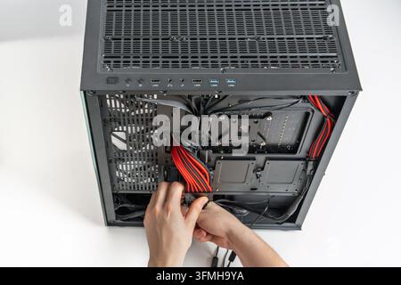 Close up view of hands installing power supply cables into a desktop computer motherboard inside a black chassis. Professional PC building process iso Stock Photo
