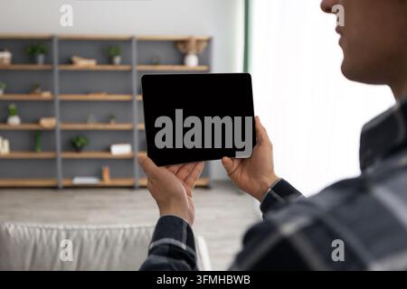 Guy Holding Digital Tablet Computer With Blank Screen Over Living Room Background Standing Indoors. Designer Using Interior Design Application. Gadget Stock Photo