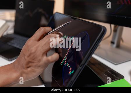 Professional trader analyzing stock market charts across multiple screens using laptop and tablet to monitor price movements, technical indicators and Stock Photo