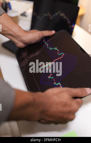 Professional financial analyst reviewing stock market charts across multiple screens using a tablet, laptop and calculator to evaluate price movements Stock Photo