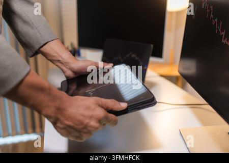 Professional financial analyst reviewing stock market charts across multiple screens using a tablet, laptop and calculator to evaluate price movements Stock Photo