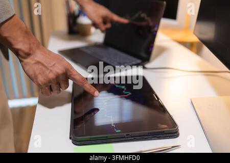 Professional financial analyst reviewing stock market charts across multiple screens using a tablet, laptop and calculator to evaluate price movements Stock Photo