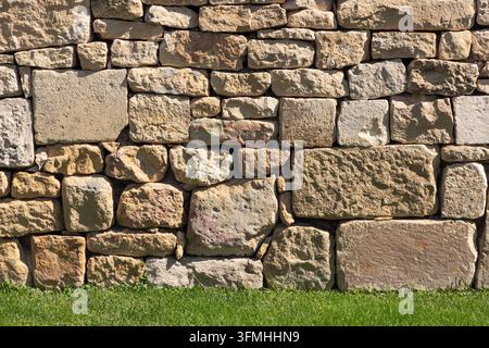 Rough old stone wall texture with green grass foreground Stock Photo
