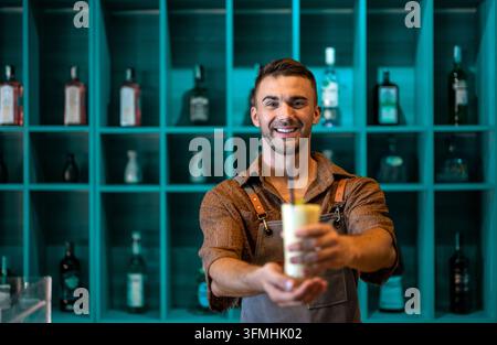 Young smiling handsome man waiter serving fruit juice, smoothie while working in a cafe. Stock Photo