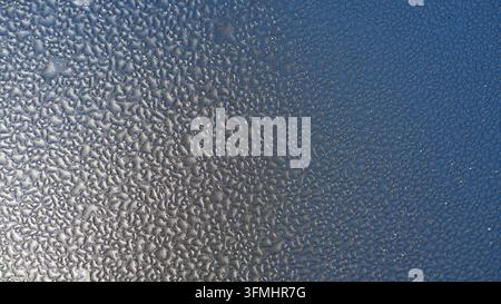 Frosty condensation beads on cold glass surface. Smooth gradient from bright to dark blue tones. Textured pattern evokes winter chill or humid morning Stock Photo