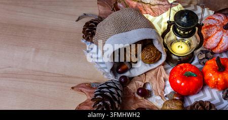 Autumn composition with walnuts, acorns, pumpkins, pine cones, and a lit lantern on a wooden table Stock Photo