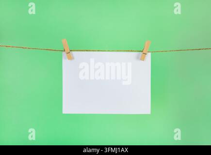 Blank note paper hanging on a clothesline on a green background Stock Photo