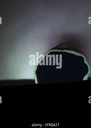 Anonymous person wearing a hooded sweatshirt using a laptop in a dark room at night. Concept of cybersecurity, hacker, online privacy, internet securi Stock Photo