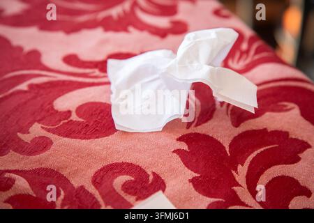 Crumpled white tissue on red patterned fabric with softly blurred background, warm indoor lighting, closeup texture detail, quiet everyday household Stock Photo