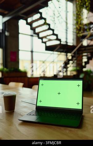 Laptop with Green Screen Display on Wooden Desk in Coworking Office Stock Photo