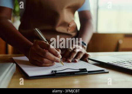 Black Woman Writing on Clipboard Managing Business Inventory Stock Photo
