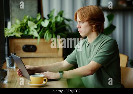 Man Working on Laptop Computer While Sitting at Modern Cafe Table Stock Photo