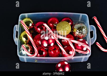 A collection of holiday decorations including shiny ornaments and striped candy canes arranged inside a transparent container on black background. Stock Photo