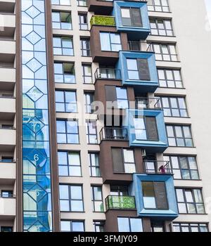 Low angle close-up of a modern skyscraper facade featuring unique blue cube-shaped windows and a glass elevator shaft. Stock Photo