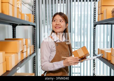 Female warehouse employee managing inventory, inspecting parcel boxes, organizing stock, and handling daily warehouse operations in a modern storage f Stock Photo