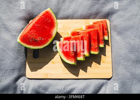 A watermelon half and sliced wedges are displayed on a wooden board. Represents summer freshness. Stock Photo