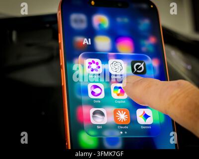 Finger touching smartphone screen with folder of AI app icons including ChatGPT, Claude, Meta AI, Grok, Dola  and Siri Stock Photo
