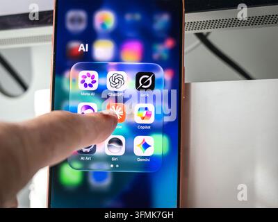 Finger touching smartphone screen with folder of AI app icons including ChatGPT, Claude, Meta AI, Grok, Copilot, and Siri Stock Photo