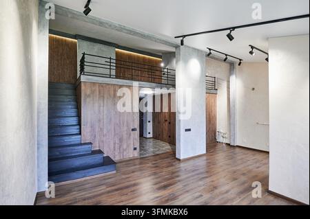 Empty contemporary living space with upper gallery, dark stairs and concrete style columns. Stylish two level home interior, architecture and modern property concept Stock Photo