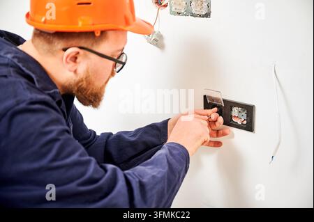 Electrician installing power outlet module and securing socket mechanism in wall. Close up of finishing stage electrical installation, wiring setup and home renovation concept Stock Photo