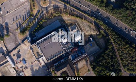 Aerial view of a large industrial facility with a flat roof, parking areas, and adjacent highway in Longcross, England, United Kingdom. Stock Photo