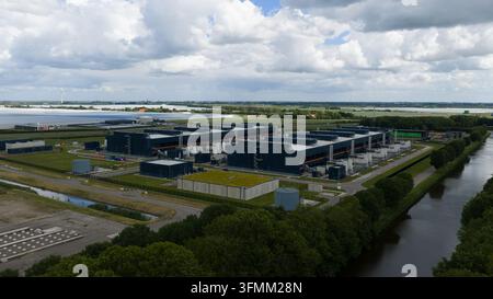 Aerial view of a large data center complex with dark industrial buildings, green roofs, and surrounding fields under a cloudy sky in Middenmeer, North Stock Photo