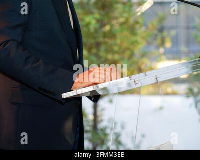 Man in suit speaking or presenting at a clear acrylic podium outdoors. Stock Photo